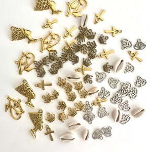 May include: Assortment of gold and silver charms, including crowns, ankh symbols, lotus flowers, and the Eye of Horus. There are also several white seashells.