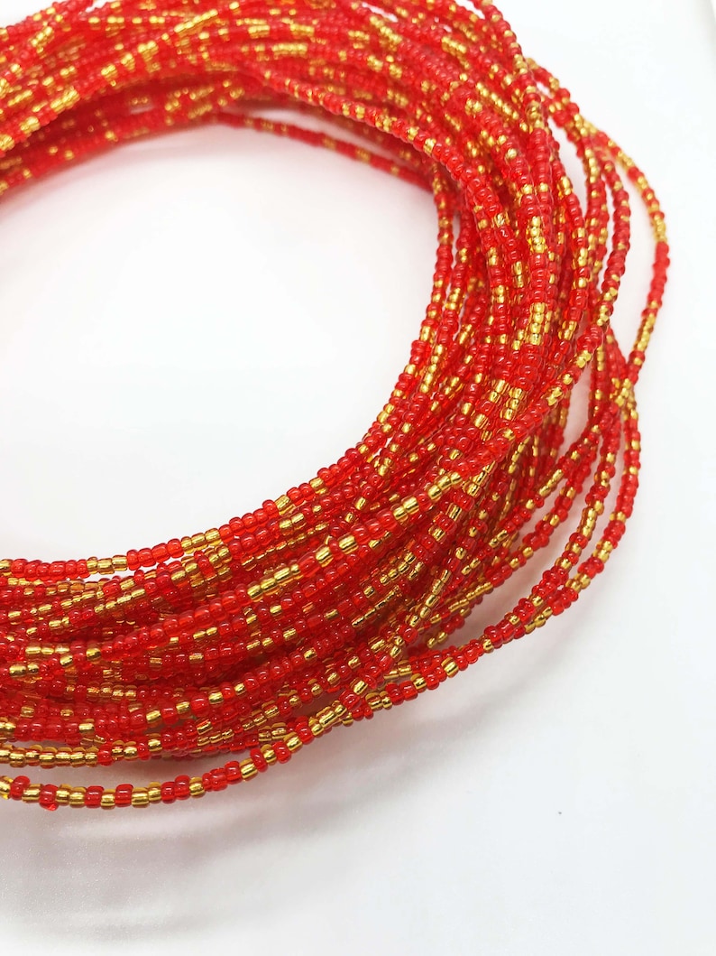 May include: A red and gold beaded waist bead, also known as a waist chain or belly chain. The beads are small and tightly woven together, creating a smooth and elegant look.
