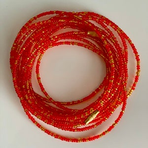 May include: A red and gold beaded waist chain with a gold clasp. The chain is made of small, round beads and is wrapped around itself to form a circle.