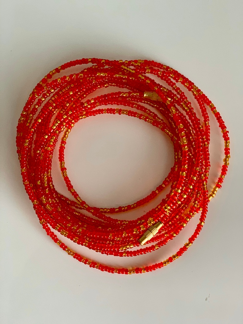 May include: A red and gold beaded waist chain with a gold clasp. The chain is made of small, round beads and is wrapped around itself to form a circle.