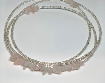 Op de afbeelding: Een zilveren kralen tailleketting met roze rozenkwarts stenen. De ketting is gelaagd en heeft een delicate uitstraling.