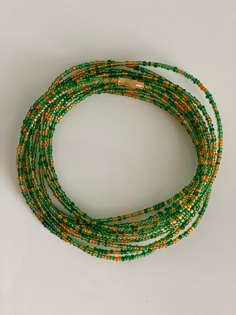 May include: A green and gold beaded waist chain with a gold clasp. The chain is made of small, round beads and is approximately 76 cm long.