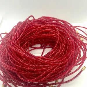 May include: A close-up of a large spool of red beads. The beads are small and round, and they are wound tightly together. The spool is made of a clear plastic material, and it has a gold metal cap on each end.