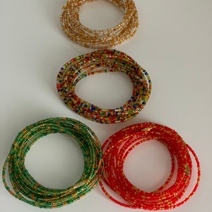 May include: Four beaded waist beads in different colours: gold, red, green, and multi-coloured. The beads are strung together in a circular shape and are approximately 76 cm in length.