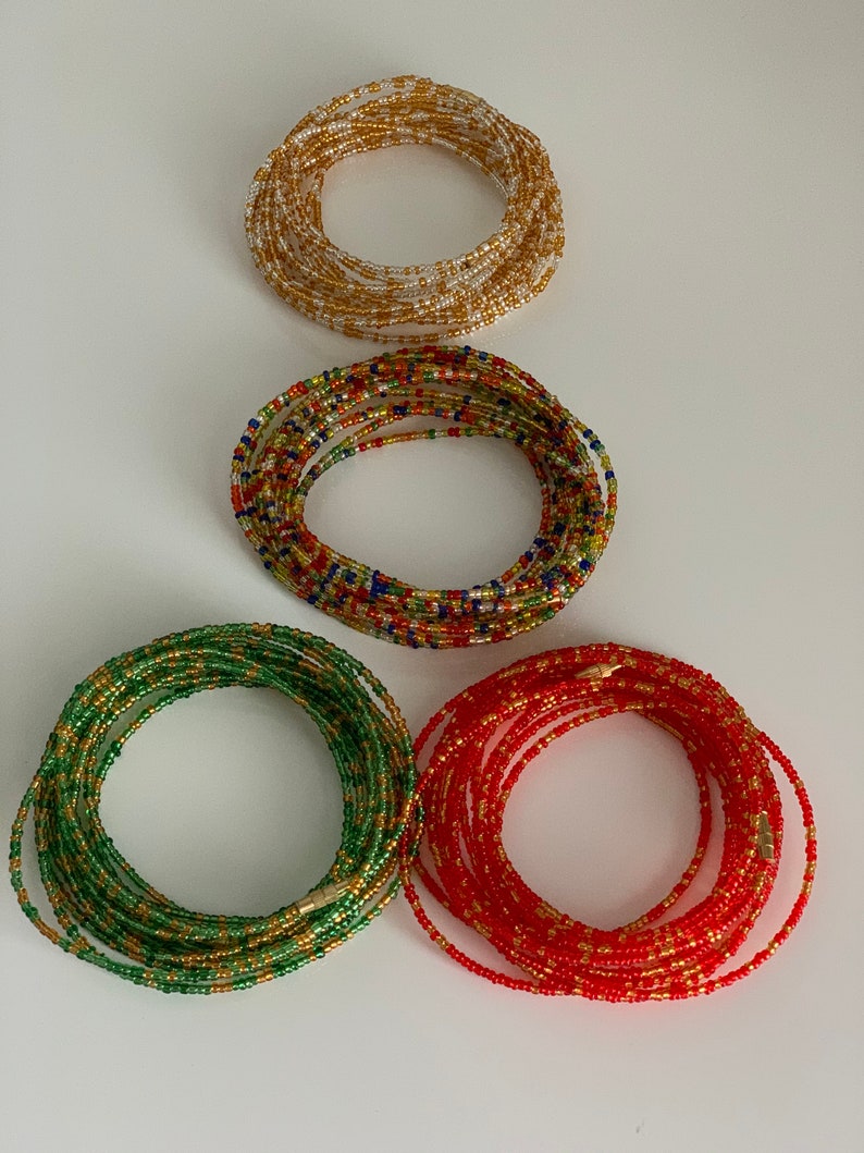 May include: Four beaded waist beads in different colours: gold, red, green, and multi-coloured. The beads are strung together in a circular shape and are approximately 76 cm in length.