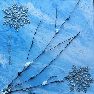 May include: A blue and white abstract painting with silver glitter snowflakes and branches. The word "WINTER" is written vertically in silver glitter on the left side of the painting.