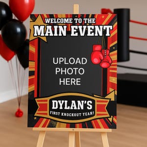 May include: A boxing-themed sign on an easel, featuring the text "WELCOME TO THE MAIN EVENT" and "DYLAN'S FIRST KNOCKOUT YEAR!". The sign has a black background with red and gold accents, and includes space to upload a photo.