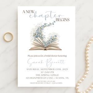 May include: White bridal shower invitation with the text "A New Chapter Begins." The invitation features an open book with blue and white floral accents. A gold ring and a pearl necklace are also visible.