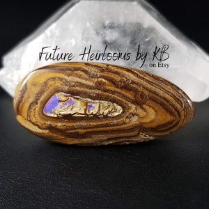 Könnte beinhalten: Ein brauner und goldener Opal mit einem violetten und blauen irisierenden Schimmer. Der Opal ist oval geformt und hat eine glatte, polierte Oberfläche. "Future Heirlooms by KB on Etsy" ist in schwarzer Schrift auf weißem Hintergrund geschrieben.