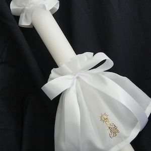 Op de afbeelding: Een witte doopkaars met een wit satijnen lint en strik. De kaars heeft een geborduurd ontwerp in goud van een zon en druiven.