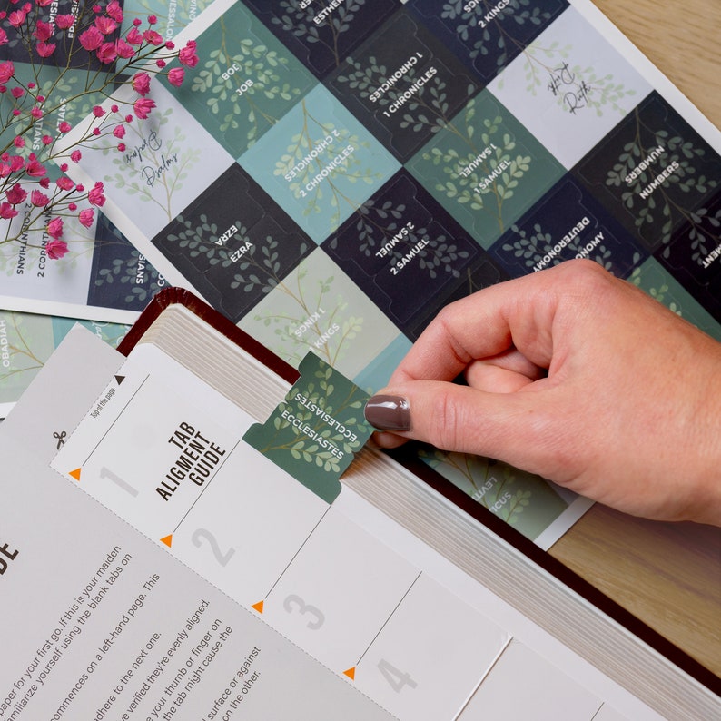 Puede incluir: Un primer plano de una gu&iacute;a para alinear las pesta&ntilde;as de la Biblia. La gu&iacute;a est&aacute; impresa en papel blanco con acentos naranja y negro. La gu&iacute;a muestra cuatro pasos numerados para alinear las pesta&ntilde;as. Se muestra una mano colocando una pesta&ntilde;a de la Biblia verde con la palabra "Eclesiast&eacute;s" impresa en ella.