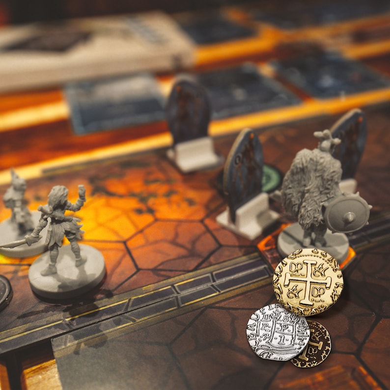 May include: A close-up of a game board with three gold and silver coins. The coins have a cross design and are on a brown and orange game board with a gray miniature figure.