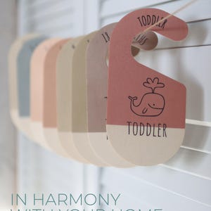 May include: A set of colorful,  hanging closet dividers with whale illustrations and the text "Toddler" on them. The dividers are made of cardboard and are strung together with twine.