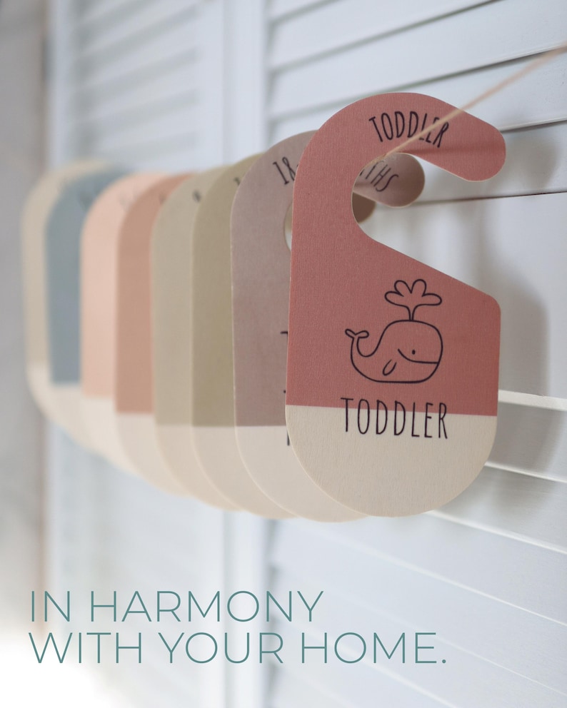May include: A set of colorful,  hanging closet dividers with whale illustrations and the text "Toddler" on them. The dividers are made of cardboard and are strung together with twine.