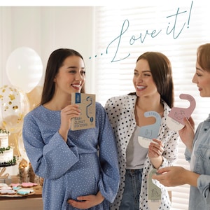 May include: Three women at a baby shower, one is pregnant and holding a book titled "Baby Closet Dividers", the other two are holding pink and blue closet dividers with different age ranges printed on them, such as "0-3 Months", "Toddler", and "Newborn".