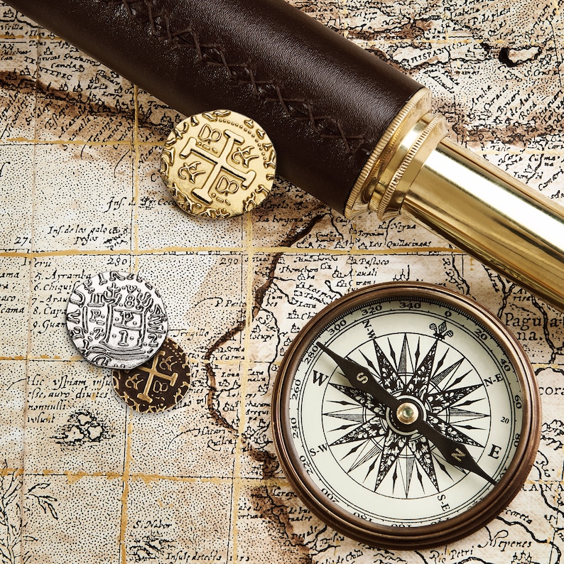 May include: A vintage compass with a black needle pointing north, surrounded by a gold-colored map with a leather-bound telescope and gold coins.