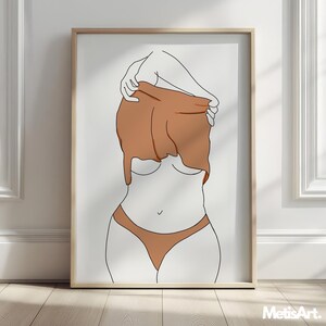May include: A framed art print featuring a minimalist line drawing of a figure partially obscured by a brown garment. The artwork depicts a person in a nude-colored bikini, with the upper body and arms in outline. The print is in a light-colored wooden frame.