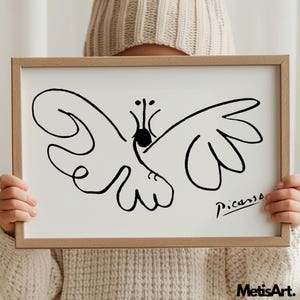 May include: A framed print featuring a black line drawing of a butterfly on a white background. The artwork includes a signature that reads Picasso in the bottom right corner. The frame is made of light-colored wood with a simple, clean design.
