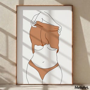 May include: Minimalist art print featuring a line drawing of a figure partially undressing. The artwork uses a palette of white, brown, and black. The figure is wearing brown underwear and a brown top. The artwork is framed in a wooden frame.