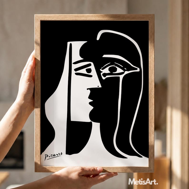 May include: A framed black and white print featuring a high-contrast abstract portrait with bold lines and geometric shapes. The artwork displays a stylized face with a prominent eye and nose, signed Picasso in the bottom left corner, encased in a light wood frame.