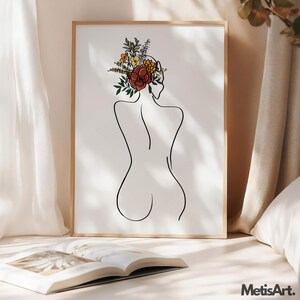 May include: A framed wall art print featuring a black line drawing of a person's back with a bouquet of colorful flowers in shades of red, orange, yellow, and green resting on the head. The artwork is displayed in a light wood frame.