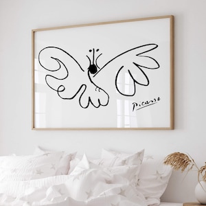 May include: A framed wall art print featuring a black line drawing of a butterfly on a white background. The artwork includes the signature Picasso in the bottom right corner. The frame is made of light-colored wood and is rectangular in shape.