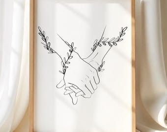 May include: A framed wall art print featuring a black line drawing of two hands holding each other, with delicate leafy vine illustrations wrapping around the wrists. The artwork is set against a plain white background within a light wood frame.