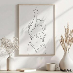K&ouml;nnte beinhalten: Ein gerahmter Schwarz-Wei&szlig;-Kunstdruck. Das Kunstwerk zeigt eine Person in Unterw&auml;sche und einem Hemd, die den Arm mit dem ausgestreckten Mittelfinger hebt. Der Druck ist in einem hellen Holzrahmen. Der Text "MetisArt." befindet sich in der unteren rechten Ecke.