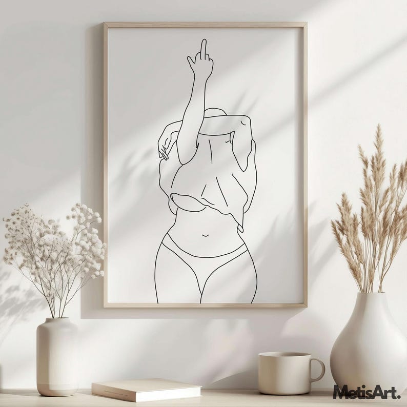 K&ouml;nnte beinhalten: Ein gerahmter Schwarz-Wei&szlig;-Kunstdruck. Das Kunstwerk zeigt eine Person in Unterw&auml;sche und einem Hemd, die den Arm mit dem ausgestreckten Mittelfinger hebt. Der Druck ist in einem hellen Holzrahmen. Der Text "MetisArt." befindet sich in der unteren rechten Ecke.