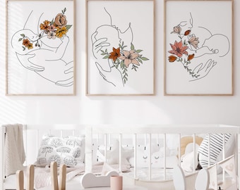 Puede incluir: Tres impresiones artísticas enmarcadas con dibujos lineales de una madre y un bebé con detalles florales. La obra de arte en blanco y negro presenta flores naranjas, rosas y amarillas. Las impresiones se exhiben sobre una cuna blanca.