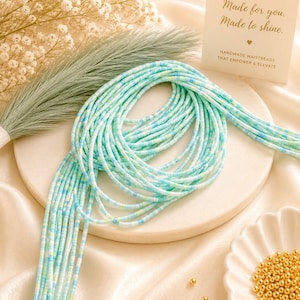 May include: A strand of waist beads featuring a mix of light blue, turquoise, and white cylindrical beads. A small white card displays the text BEADBUTIK, Made for you. Made to shine., and HANDMADE WAISTBEADS THAT EMPOWER & ELEVATE.