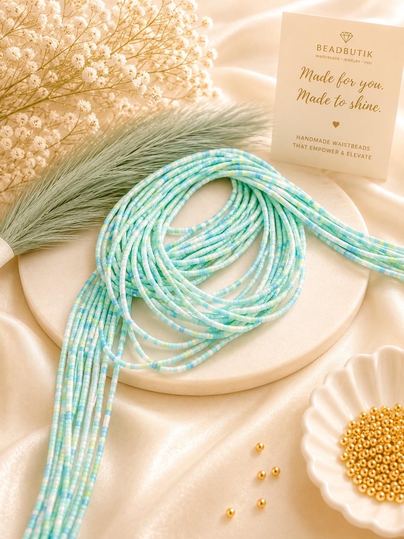 May include: A strand of waist beads featuring a mix of light blue, turquoise, and white cylindrical beads. A small white card displays the text BEADBUTIK, Made for you. Made to shine., and HANDMADE WAISTBEADS THAT EMPOWER & ELEVATE.