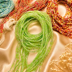 May include: A collection of waist beads featuring multiple strands of small glass beads in various colors including lime green, orange, yellow, pink, and blue, accented with metallic silver spacers and finished with white cotton tie strings.