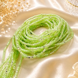 May include: A coiled strand of waist beads featuring translucent light green glass beads interspersed with small, reflective silver-colored metallic spacers. The beads are arranged in a continuous circular pattern, creating a vibrant and textured appearance.
