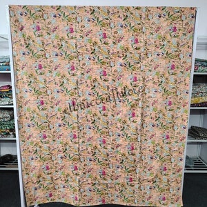 May include: A peach-colored kantha quilt with a floral pattern. The quilt is made of cotton and is hand-stitched. It is a traditional Indian textile.