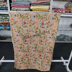 May include: A peach-colored kantha quilt with a floral pattern. The quilt is made of cotton and is hand-stitched. It is a traditional Indian textile.