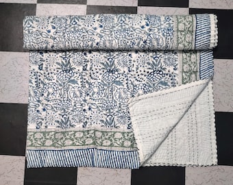 Puede incluir: Una colcha de algodón blanco con un estampado floral azul y verde. La colcha está doblada por la mitad y tiene un respaldo blanco.