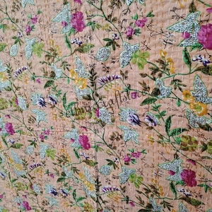 May include: A peach-colored kantha quilt with a floral pattern in shades of pink, green, and white. The quilt is hand-stitched with a running stitch, creating a delicate and intricate design.