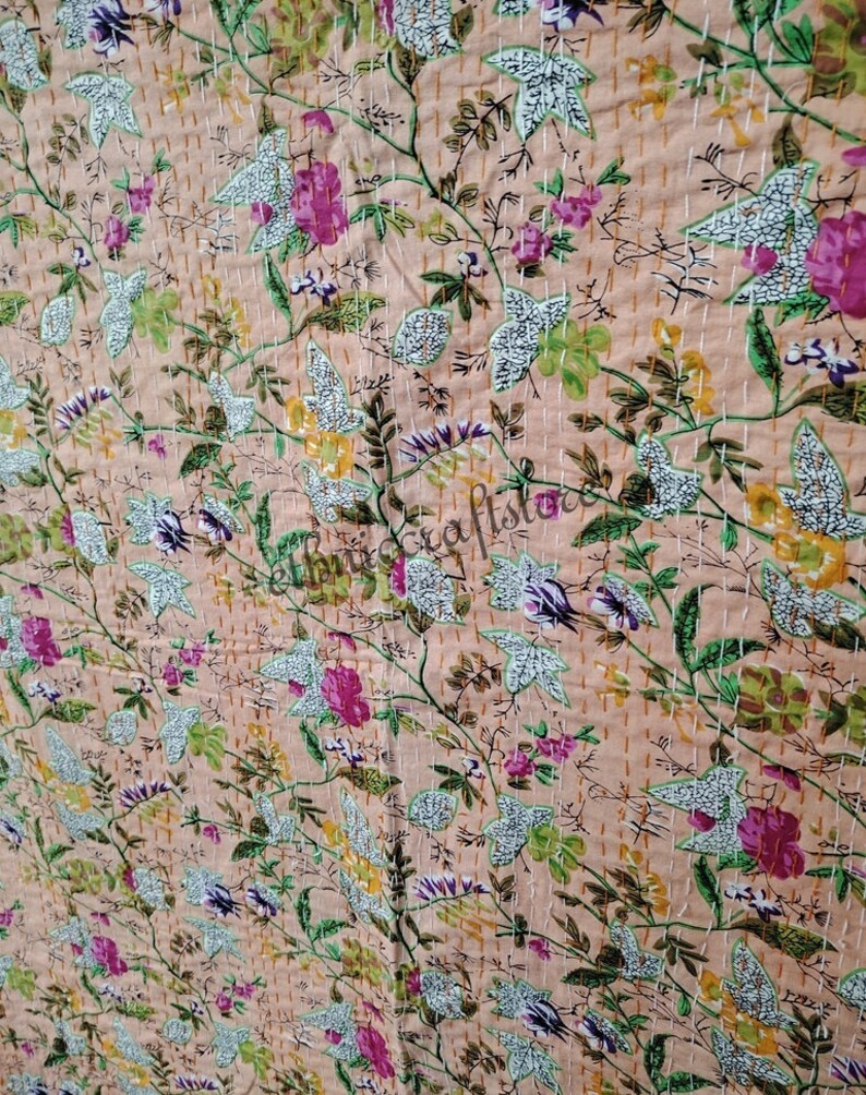 May include: A peach-colored kantha quilt with a floral pattern in shades of pink, green, and white. The quilt is hand-stitched with a running stitch, creating a delicate and intricate design.