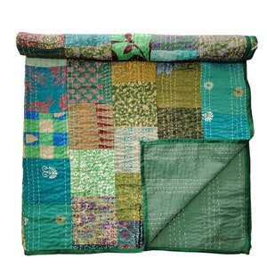 May include: A green patchwork quilt made from various fabrics with floral and geometric patterns. The quilt is folded in half and has a green border.