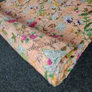 May include: A close-up of a peach-colored fabric with a floral pattern. The fabric is folded and has a textured surface. The text "ethniccraftstore" is visible on the fabric.