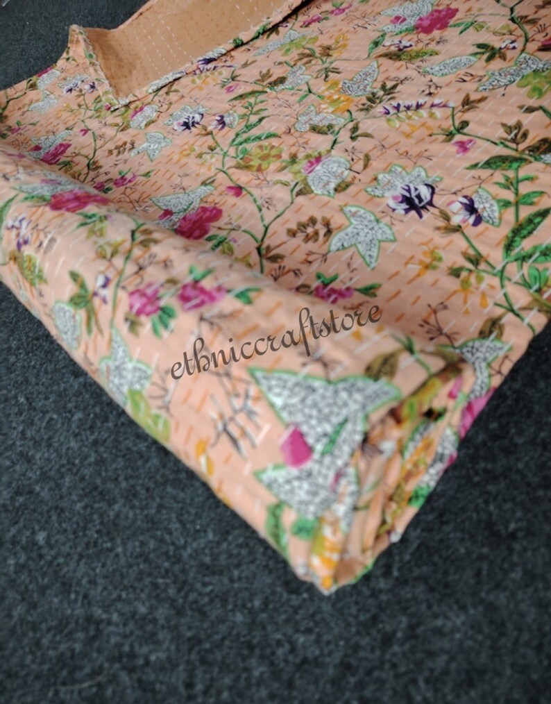 May include: A close-up of a peach-colored fabric with a floral pattern. The fabric is folded and has a textured surface. The text "ethniccraftstore" is visible on the fabric.