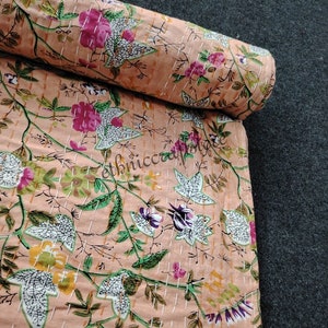 May include: A peach-colored fabric with a floral print featuring white, pink, green, and yellow flowers. The fabric is rolled up and has a white stitching pattern.