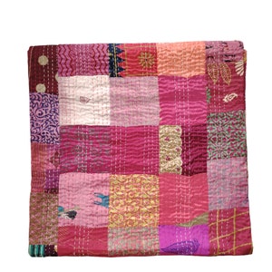 May include: A pink and purple patchwork quilt with a variety of floral and geometric patterns. The quilt is made of different fabrics and is stitched together with a running stitch.