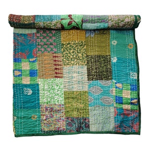 Peut inclure: Une courtepointe en patchwork composée de différents tissus dans des tons de vert, bleu et marron. La courtepointe est composée de carrés de motifs et de couleurs différents, et est cousue avec du fil blanc. La courtepointe est enroulée et prête à être utilisée.