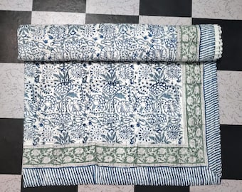 Könnte beinhalten: Eine weiße Baumwolldecke mit einem blauen und grünen Blumenmuster. Die Decke ist in der Mitte gefaltet und hat einen Fransenrand.