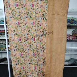 May include: A peach-colored kantha quilt with a floral print and a solid brown back. The quilt is hand-stitched and has a vintage look.
