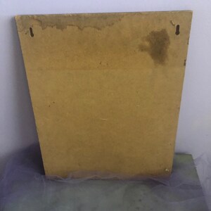 May include: A rectangular, light brown wooden board with two small metal hooks at the top for hanging. The board has a trapezoid shape and shows signs of water damage near the top edge. The background is a light purple wall.
