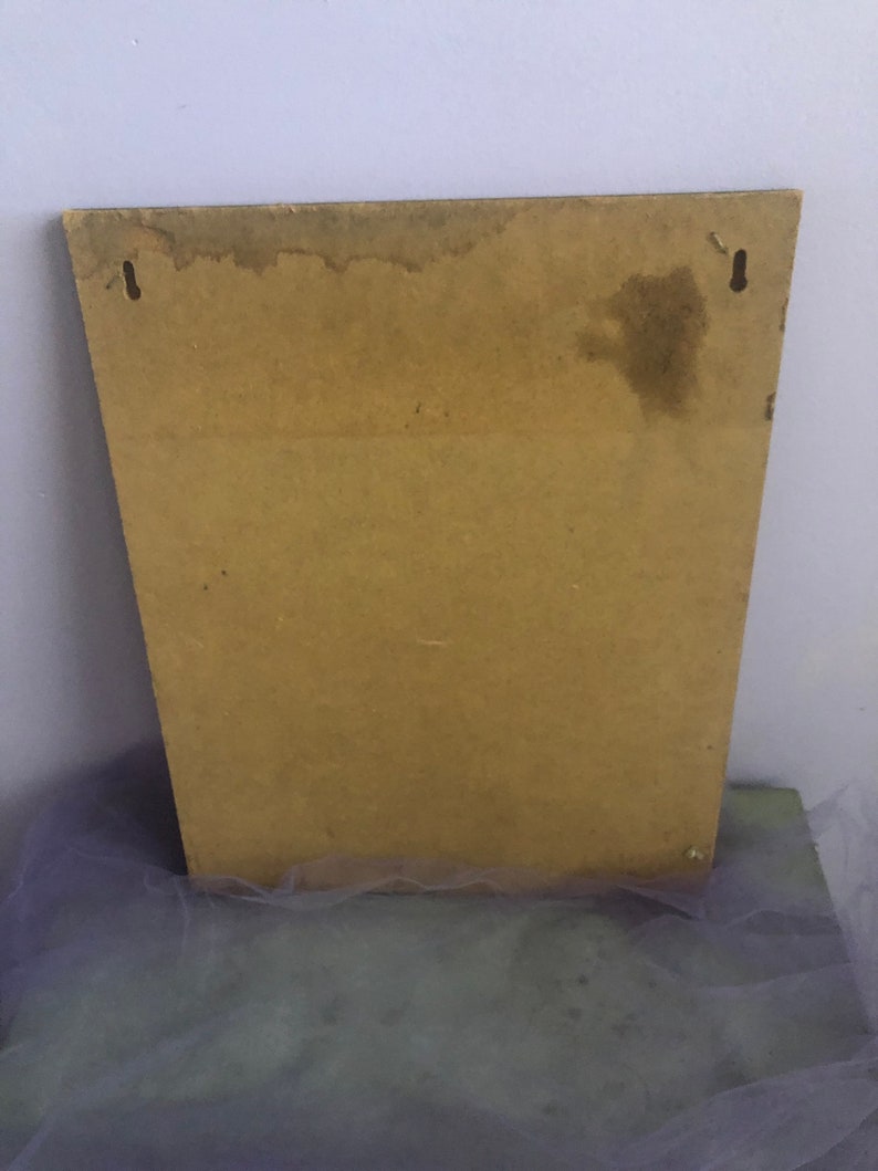May include: A rectangular, light brown wooden board with two small metal hooks at the top for hanging. The board has a trapezoid shape and shows signs of water damage near the top edge. The background is a light purple wall.