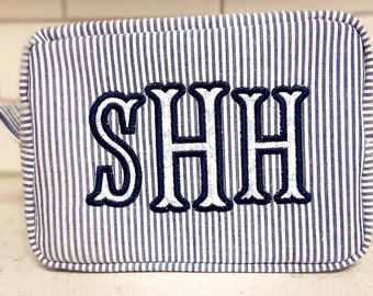 以下が含まれることがあります： 白と青のストライプの布製の化粧ポーチで、"SHH"の文字が紺色で刺繍されています。